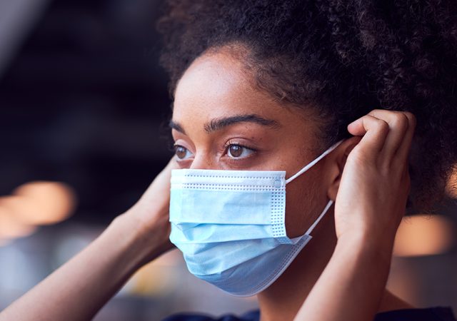 Person putting a surgical mask on their face to help prevent the spread of infection.